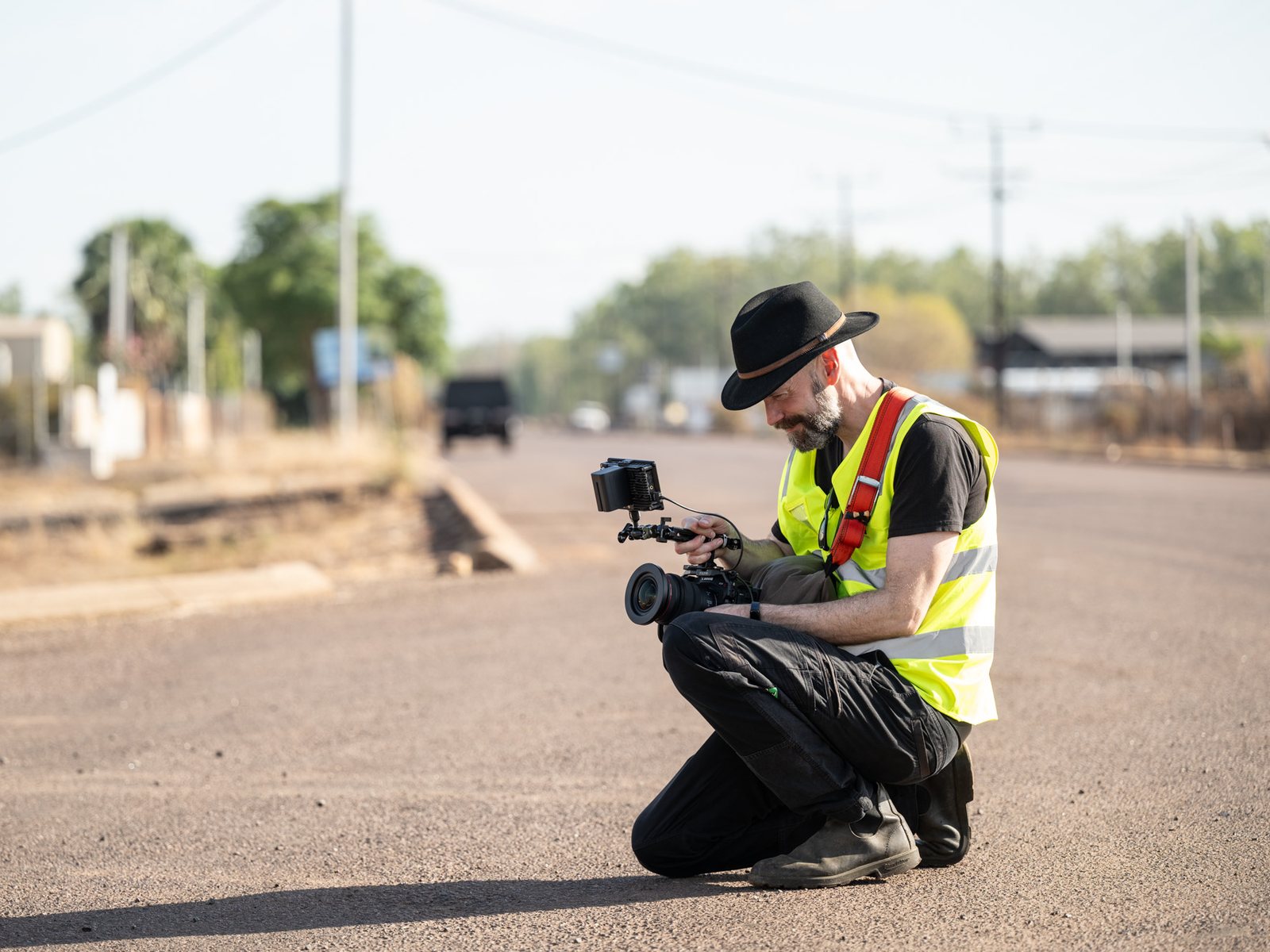 A camera operator in a hi-vis vest kneeling with a cinema camera on a dusty road in a remote town, on a Lift shoot