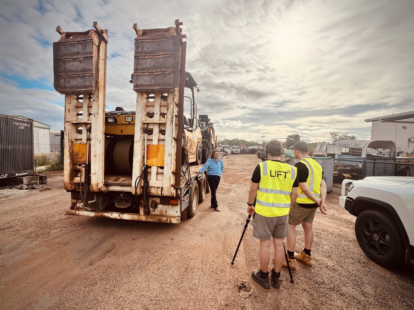 Two of the Lift crew in hi-vis vests behind a low loader in the FJ Bitumen yard