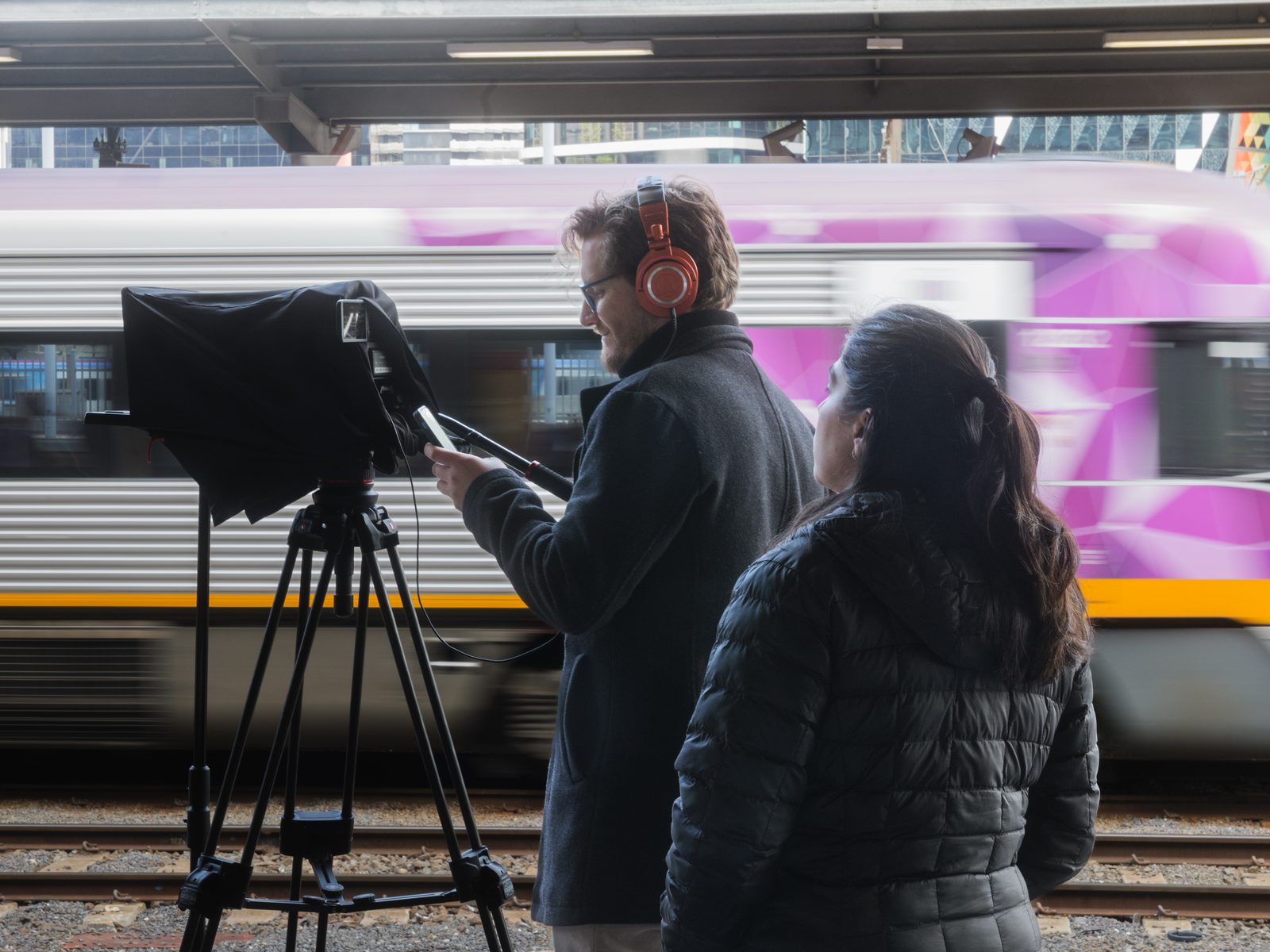 Two of the Lift crew filming on a station platform as a train passes