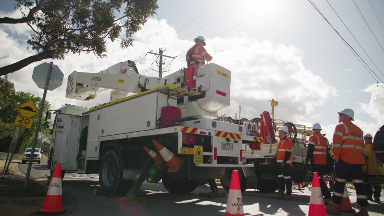 A line crew in orange hi-vis working from an elevated work platform truck on a suburban street