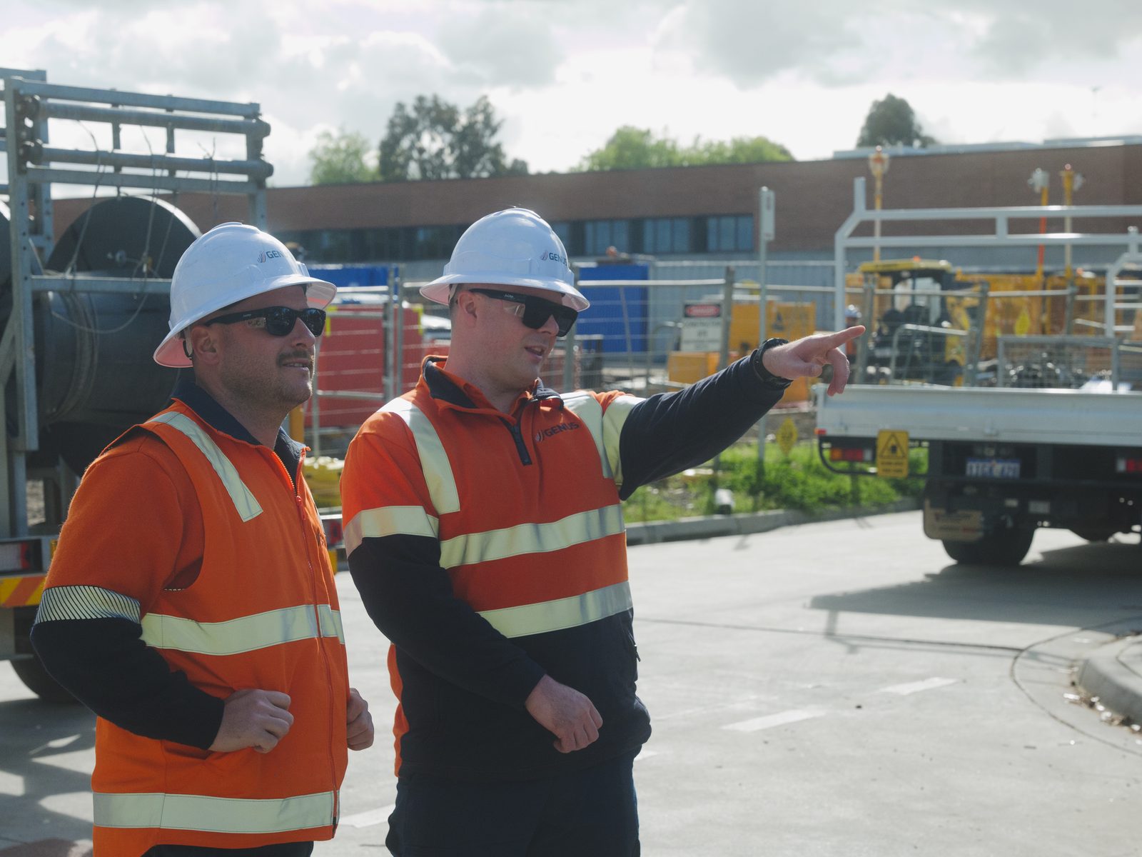 Two Genus line workers in hard hats and orange hi-vis talking through a job on site