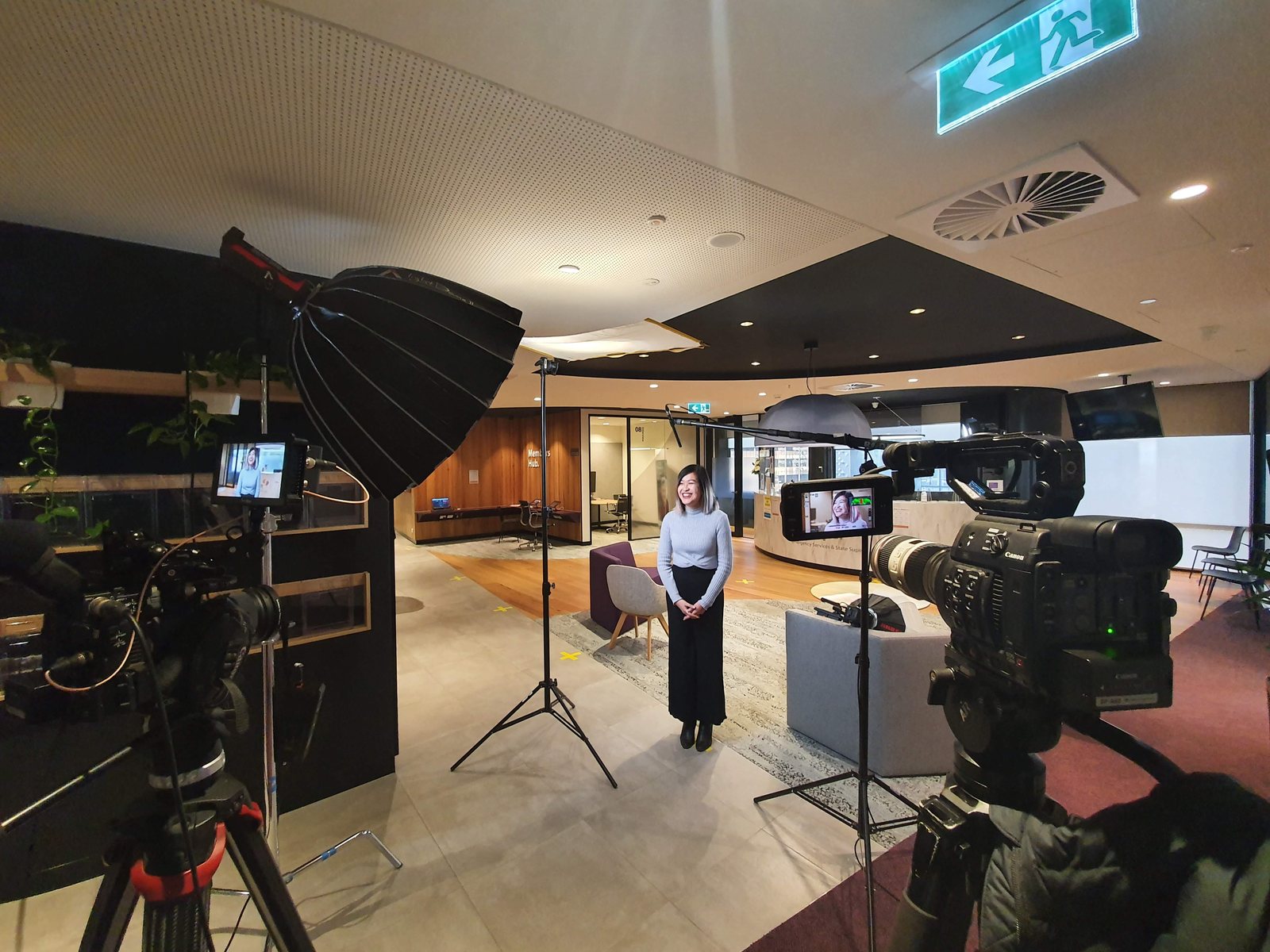 Two cameras and a softbox light set up in a modern office, with a presenter standing ready to film