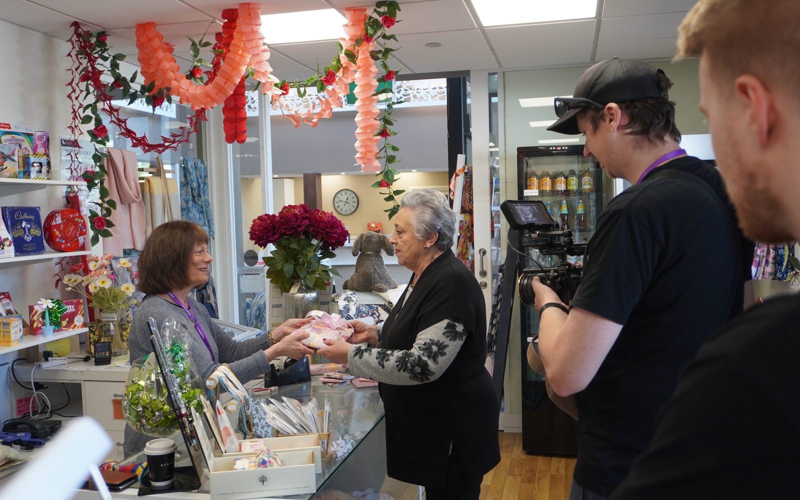 Lift filming a volunteer serving a resident at the counter of the Mayflower gift shop
