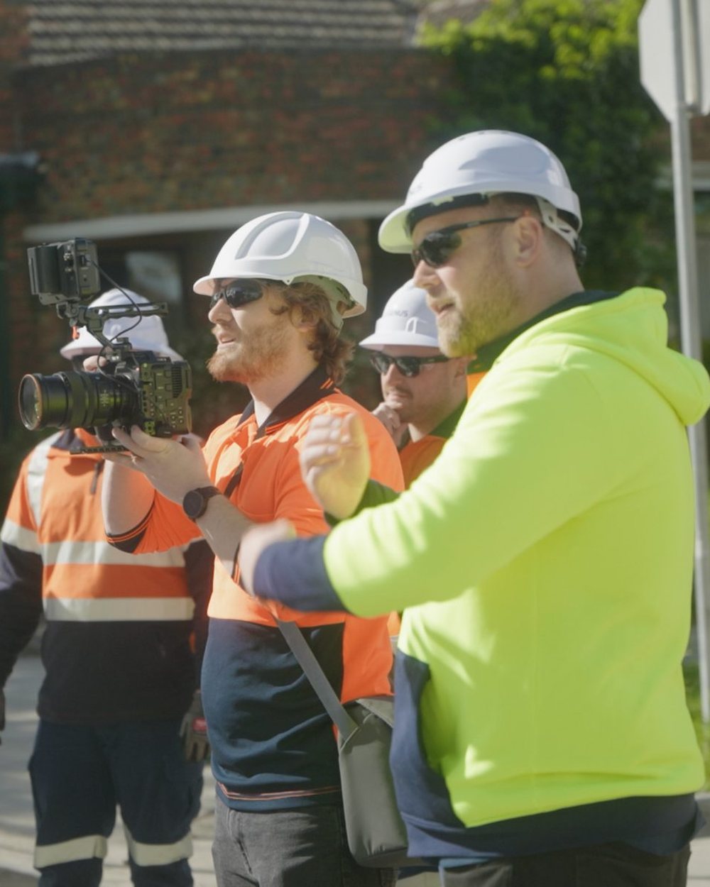 A Lift camera operator filming a Genus line crew in hard hats on a suburban street