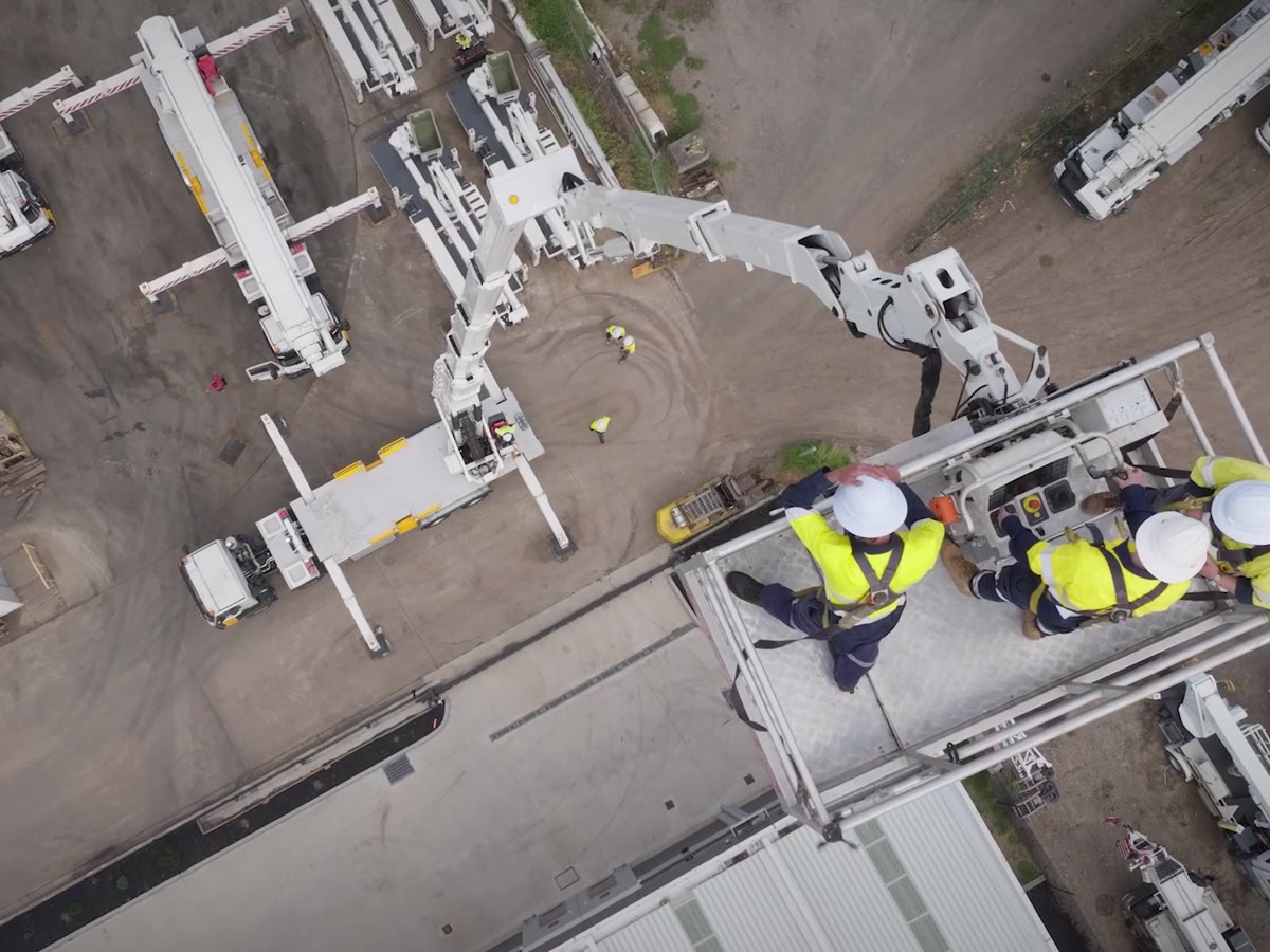 Three Genus crew in a work platform bucket seen from above, with the EWP fleet laid out below