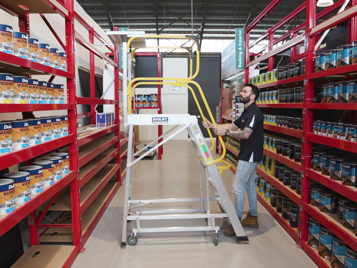 A worker positioning a platform ladder in a warehouse aisle