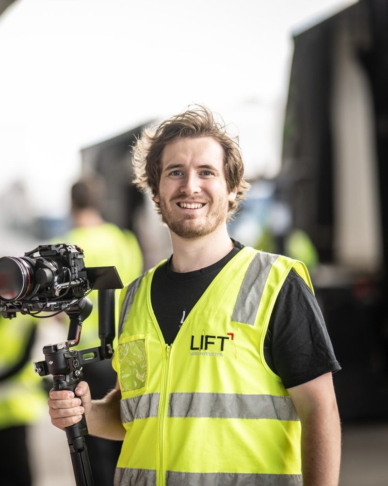 Jock Turner, Lead Videographer at Lift Video Production, holding a camera on a gimbal in a transport yard