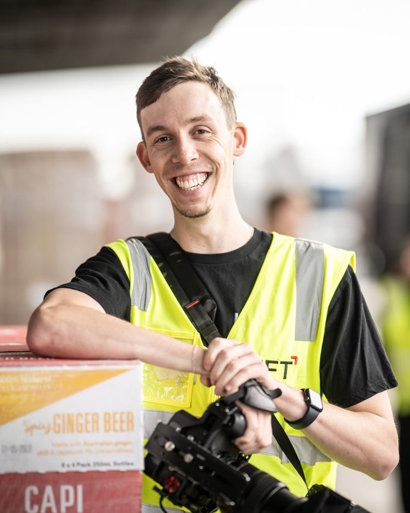 Patrick Neideck, Videographer at Lift Video Production, leaning on a pallet with a cinema camera
