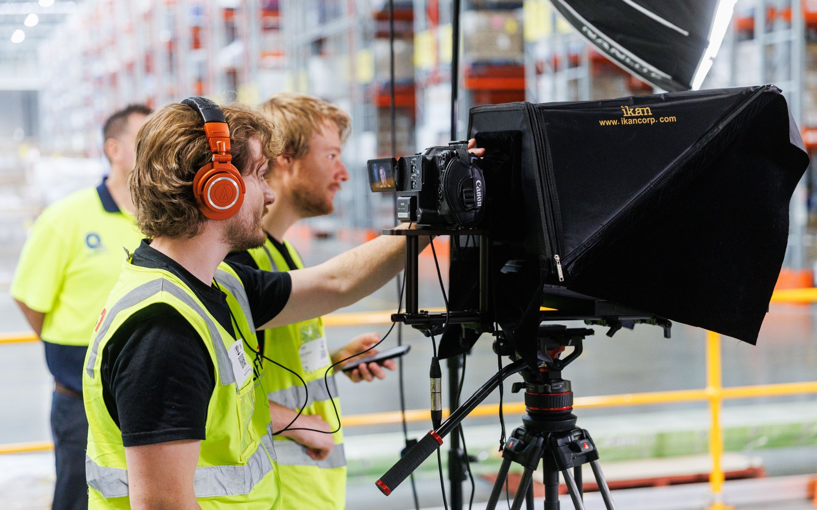 Two of the Lift crew in hi-vis setting up a camera with an autocue in a warehouse aisle